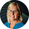 A woman with blonde hair and glasses smiles at the camera, wearing a blue top, with a dark background featuring green curved lines.